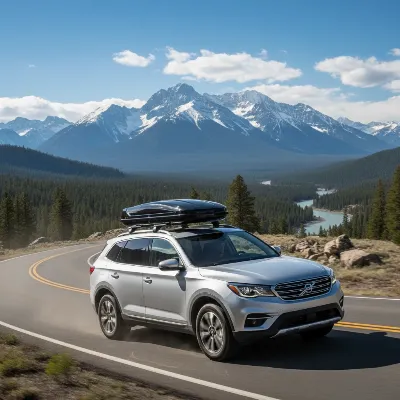 A silver SUV with a sleek, black roof rack carrying a cargo box, driving on a scenic open road under a clear sky.